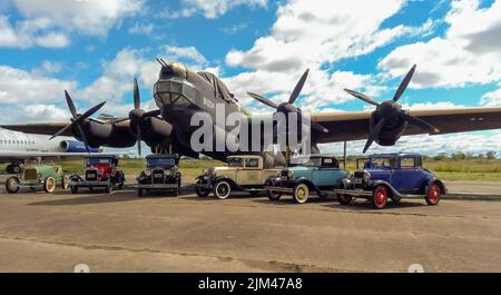 Mehrere alte Ford Model A in verschiedenen Karosserievarianten um 1930 vor einem viermotorigen Bomber Avro Lincoln MKII aus dem Zweiten Weltkrieg geparkt 1944-1967. Copyspace. Stockfoto