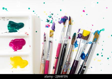 Art Paint Pinsel, Palette und bunte Splatter auf weißem Leinwandpapier Stockfoto