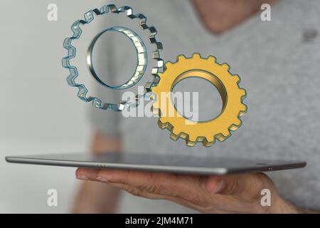 Eine Hand, die ein Tablet mit einigen illustrierenden grauen Zahnrädern hält, die über dem Display schweben. Stockfoto