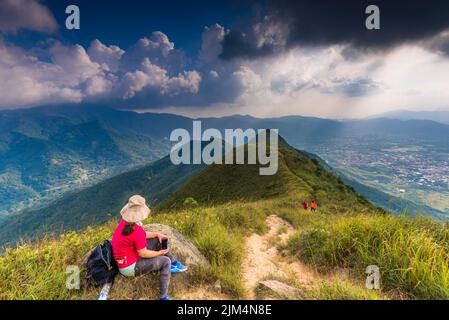Eine Wanderin Hongkong, Frau in Rot auf einem Berghang, die die wunderschöne Landschaft genießt. Stockfoto