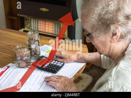 Ältere Dame in den Neunzigern, die Gas-, Strom- und Stromrechnungen mit Taschenrechner und Gläsern mit Münzen auf dem Tisch betrachtet. Gasbrand im Hintergrund. Stockfoto