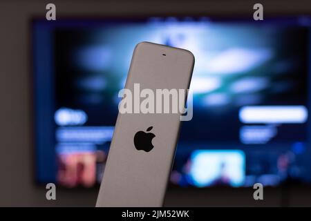 Das Apple-Logo ist auf der Rückseite einer AppleTV-Fernbedienung im Wohnzimmer zu sehen, während AppleTV+ im Hintergrund zu sehen ist. Stockfoto