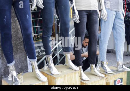 Ein Palästinenser sitzt neben Schaufensterpuppen in einem Bekleidungsgeschäft in Gaza City. Die Hamas-Führer in Gaza verhängten vor dem neuen Schuljahr eine ganze Reihe neuer Steuern auf importierte Kleidung und Büromaterialien, was begrenzte, aber seltene Proteste in der verarmten Küstenenklave auslöste. Es kommt zu einer Zeit, in der 2,3 Millionen Menschen in Gaza unter der 15 Jahre alten israelischen Blockade leiden, aber auch unter einem neuen Preisanstieg, der durch globale Lieferkettenprobleme und die russische Invasion in der Ukraine verursacht wird. Die Liste des Wirtschaftsministeriums enthält geplante Steuern auf Artikel wie verpackte Nüsse mit einem Einfuhrzoll von 2.000 Schekel Stockfoto