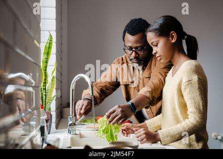 Schwarzer bärtiger Mann, der mit seiner Tochter zu Hause Sandwiches zubereitet Stockfoto