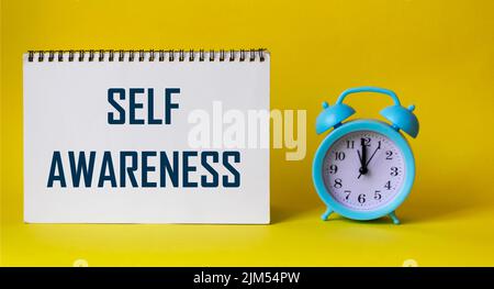 Das Wort Selbstbewusstsein auf einem Notizblock und einem gelben Hintergrund, neben der Uhr Stockfoto