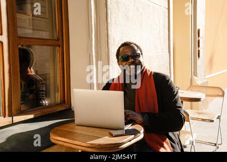 Schwarzer bärtiger Mann mit Laptop, während er im Café im Freien sitzt Stockfoto