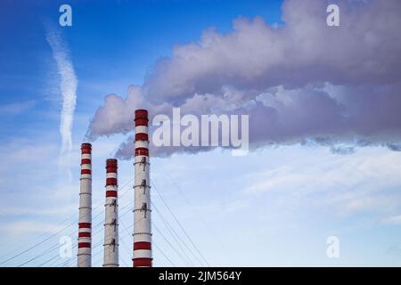 Luftverschmutzung. Starker Rauch aus Schornsteinen in Industrieanlagen. Die Produktionsstätte belastet die Umwelt. Rauchenden Kamine vor blauem Himmel. Stockfoto