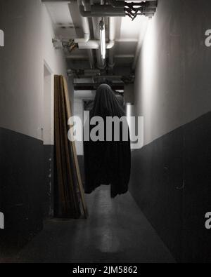 Ein 3D Render-Design einer Person, die vollständig mit einem schwarzen Mantel bedeckt ist und in einem dunklen Korridor über den Boden fliegt, Horror-Konzept Stockfoto