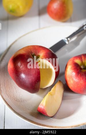 Die Hälften des roten Apfels, der ganze Apfel in weißem Teller auf dem Tisch Stockfoto