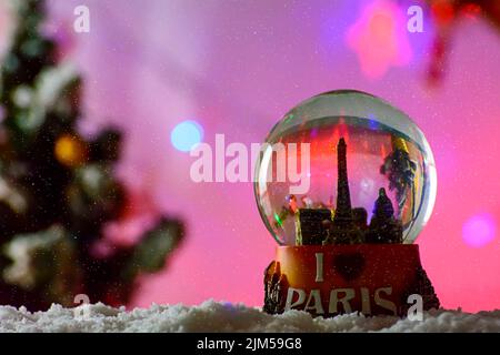 Eine Nahaufnahme schoss ein Schneekugel-Souvenir des Pariser Eiffelturms auf den Schneeflocken auf einem unscharfen violetten Hintergrund Stockfoto