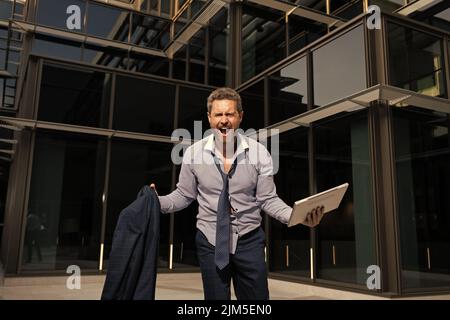 Frustrierter Geschäftsmann, der vor Wut mit Computer und Jacke schrie, Geschäftszusammenbruch Stockfoto