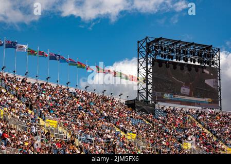 Birmingham, Großbritannien, 4.. August 2022. Zuschauer im Alexander Stadium, Birmingham, genießen die Leichtathletik bei den Commonwealth Games 2022. Flaggen der Commonwealth-Staaten fliegen über das Stadion. Leonie Beuu aus Papua-Neuguinea ist auf dem Bildschirm zu sehen. Quelle: Martin Anderson/Alamy Live News Stockfoto