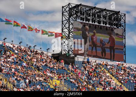 Birmingham, Großbritannien, 4.. August 2022. Zuschauer im Alexander Stadium, Birmingham, genießen die Sport Relief All-Stars Teil der Veranstaltung bei den Commonwealth Games 2022. Auf der Leinwand werden Dame Kelly Holmes und Ellie Simmonds OBE von Radzi Chinyanganya und Iwan Thomas während des Sport Relief-Events nach dem wichtigsten Althletik-Event interviewt. Flaggen der Commonwealth-Staaten fliegen über das Stadion. Quelle: Martin Anderson/Alamy Live News Stockfoto