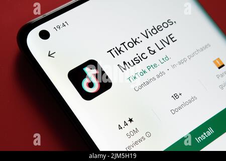 TikTok App im Google Play Store auf dem Smartphone-Bildschirm auf rotem Hintergrund angezeigt. Nahaufnahme mit selektivem Fokus. Stafford, Vereinigtes Königreich, Stockfoto