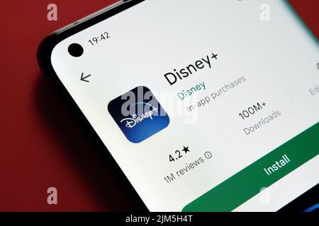 Disney Plus App im Google Play Store auf dem Smartphone-Bildschirm auf rotem Hintergrund zu sehen. Nahaufnahme mit selektivem Fokus. Stafford, United Kin Stockfoto