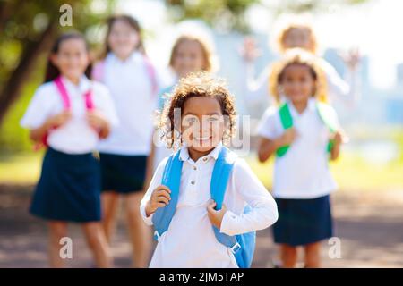 Die Kinder gehen zurück zur Schule. Interrassische Gruppe von Kindern unterschiedlichen Alters laufen und jubeln am ersten Tag des neuen akademischen Jahres. Beginn der Schulferien. Stockfoto