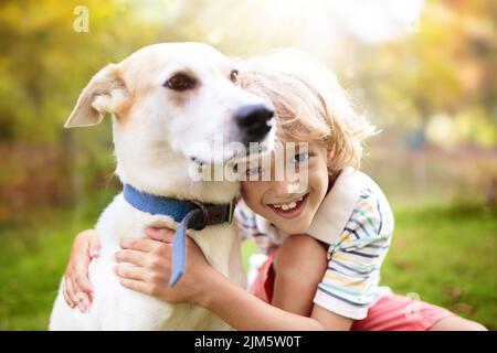 Kind spielt mit seinem Hund. Kinder und Hunde. Kleiner Junge umarmt sein Haustier im sonnigen Hinterhof. Tierpflege. Liebe und Freundschaft. Haustiere sind erlaubt. Stockfoto