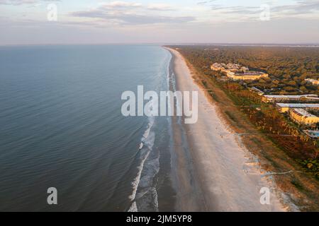 Blick aus der Vogelperspektive auf den Coligny Beach auf Hilton Head Island. Blick auf das Meer bei Sonnenuntergang mit Bäumen und Hotels im Vordergrund Stockfoto