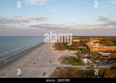 Blick aus der Vogelperspektive auf Coligny Beach auf Hilton Head Island. Meerblick bei Sonnenuntergang mit Bäumen und Hotels im Vordergrund Stockfoto