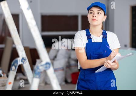 Fokussierte Bauherrin, die Papiere auf der Baustelle im Innenbereich ausfüllt Stockfoto