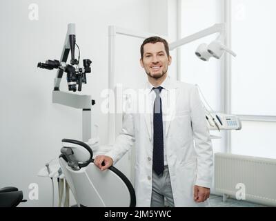 Porträt eines glücklichen männlichen Zahnarztes mit Laborkittel in der weißen Zahnklinik Stockfoto