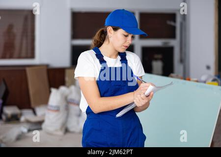 Fokussierte Bauherrin, die Papiere auf der Baustelle im Innenbereich ausfüllt Stockfoto