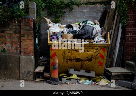 Ein voller gelber Müll, der voll Müll von einer Baustelle ist. Holz und andere Baustoffe um ihn herum. Bereit zum Loch zu gehen. Stockfoto