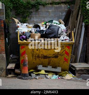 Ein voller gelber Müll, der voll Müll von einer Baustelle ist. Holz und andere Baustoffe um ihn herum. Bereit zum Loch zu gehen. Stockfoto