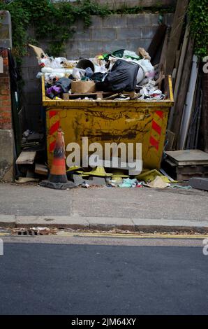 Ein voller gelber Müll, der voll Müll von einer Baustelle ist. Holz und andere Baustoffe um ihn herum. Bereit zum Loch zu gehen. Stockfoto