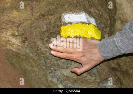 Gemaltes Wanderzeichen auf einem Felsen, das die Richtung des Weges mit nicht erkennbarer Menschenhand markiert. Stockfoto