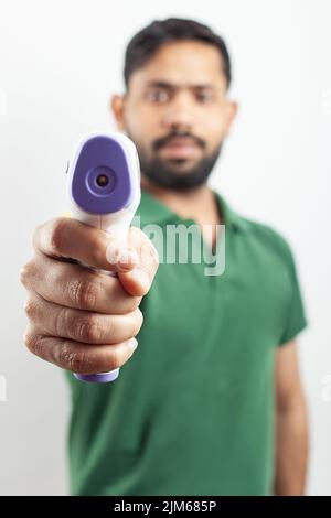 Junger, hübscher Kerl, der Infrarot-Thermometer zeigt, das die Körpertemperatur der Grippe auf weißem Hintergrund misst. Stockfoto
