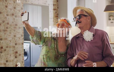 Sagen Sie Käse. Ein glückliches Seniorenpaar, das in Kostümen zusammensteht und mit einem Handy Selfies macht. Stockfoto