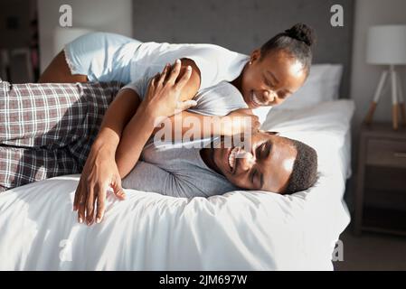 Machen Sie es sich zur Gewohnheit, verspielt und albern zusammen zu sein. Ein liebevolles junges Paar, das sich zu Hause auf dem Bett entspannt. Stockfoto