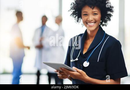 Krankenschwester oder Ärztin mit einer Tablette und Kollegen im Hintergrund. Selbstbewusster, lächelnder Gesundheitsexpert, der mit der Medizin zusammenarbeitet Stockfoto