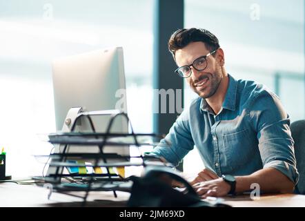 Selbstbewusste, entspannte und glückliche, professionelle Führungskraft oder HR-Assistentin, die in einem modernen Büro am Computer arbeitet. Lächelnd, stolzer Mann tippt und antwortet Stockfoto