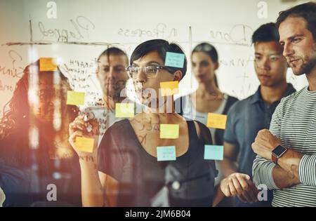Geschäftsleute, die Ideen auf einem Glasbrett planen, denken, Brainstorming durchführen und an einer Strategie für ein Projekt arbeiten. Intelligente, beschäftigte und organisierte Mitarbeiter Stockfoto