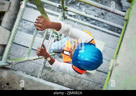 Je härter du arbeitest, desto höher gehst du. Eine junge Frau klettert auf einer Baustelle eine Leiter hinauf. Stockfoto
