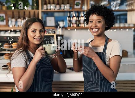 Wir haben uns über Kaffee gefrecht. Porträt zweier junger Frauen, die gemeinsam Kaffee trinken, während sie in einem Café arbeiten. Stockfoto