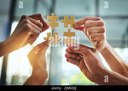 Gruppe von Geschäftsleuten, die Puzzleteile halten. Im Bürogebäude verbinden sich Profis und arbeiten zusammen. Nahaufnahme der Hände und des Teams Stockfoto