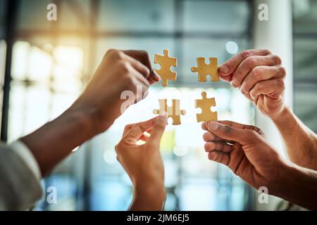 Gruppe von Geschäftsleuten, die Puzzleteile halten. Im Bürogebäude verbinden sich Profis und arbeiten zusammen. Nahaufnahme der Hände und des Teams Stockfoto