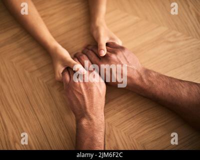 Ein Paar hält die Hände, die Liebe, Romantik und Unterstützung zeigen, während es von oben an einem Tisch sitzt. Draufsicht auf einen liebevollen Ehemann und eine liebevolle Frau, die sich liebevoll teilen Stockfoto