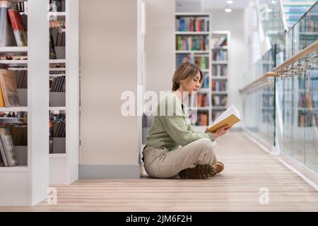 Nachdenkliche Frau mittleren Alters mit Buch, die Freizeit in der Bibliothek verbringt und gerne liest Stockfoto