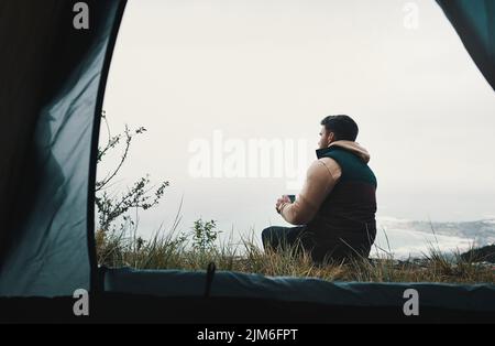 Nicht alle Klassenzimmer haben vier Wände. Rückansicht eines jungen Mannes, der während des Campens in der Wildnis Kaffee trinkt. Stockfoto