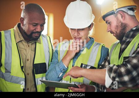 Spitzentechnologie für hochwertige Konstruktion. Eine Gruppe von Bauherren, die auf einer Baustelle mit einem digitalen Tablet arbeiten. Stockfoto