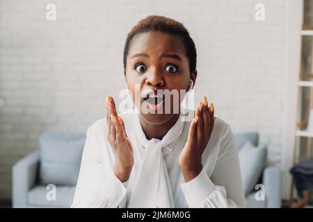 Die Afro-Frau, die mit weit geöffneten Augen im Bürozentrum saß, erhielt unglaubliche Nachrichten. Unglaublicher Ausdruck. Nachrichten oder Daten online abrufen. Stockfoto