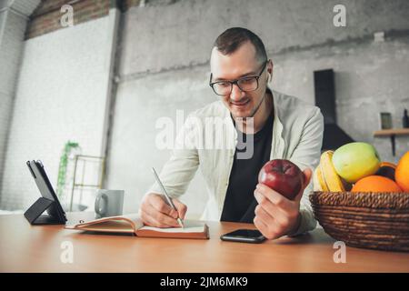 Ein Geschäftsmann, der mit kabellosen Geräten im Notebook schrieb, während er morgens zu Hause frühstücken musste. Essen und Entspannen. Internet-Fernbedienung verwenden Stockfoto