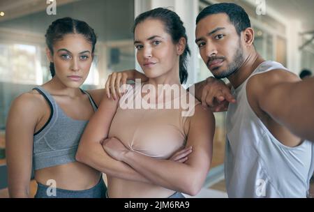 Wir halten uns gegenseitig motiviert. Beschnittenes Porträt von drei jungen Athleten, die im Fitnessstudio zusammen stehen. Stockfoto