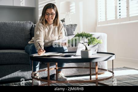 Erfolg liegt in den kleinen Dingen, die Sie tun. Eine junge Frau, die Papierkram betrachtet, während sie von zu Hause aus arbeitet. Stockfoto