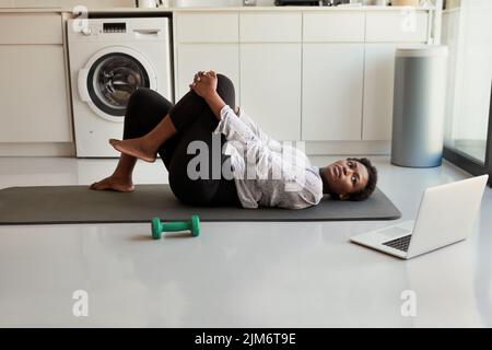 Mache ich das richtig? Eine junge Frau, die einen Laptop benutzt, während sie zu Hause trainiert. Stockfoto