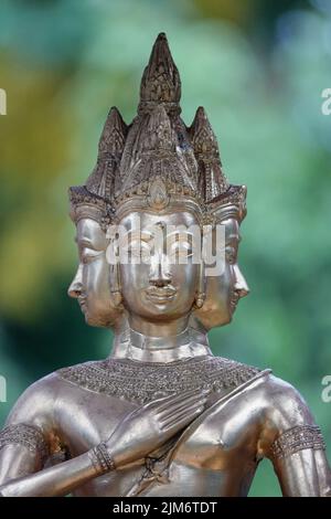 Eine vertikale Aufnahme einer silbernen, dreiköpfigen Buddha-Statue mit verschwommenem Grün im Hintergrund Stockfoto